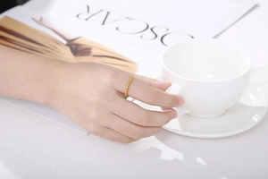 Close-up of a gold twisted rope ring worn while holding a white coffee cup