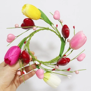 Handheld view of a colorful artificial tulip and heart bead candle ring with green leaves