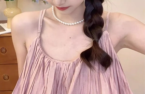 Détail d'un caraco plissé rose associé à un collier de perles blanches à un seul rang