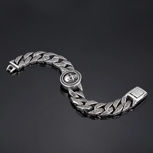 Macro shot of silver skull charm link bracelet with Greek key patterns on a dark background