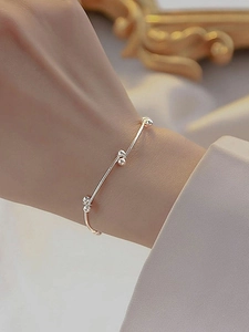 Detail view of a minimalist silver beaded knot bracelet worn on a wrist for an elegant look