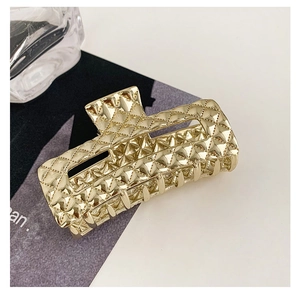 Macro detail of golden rectangular hair claw clip with a quilted pattern and metallic finish