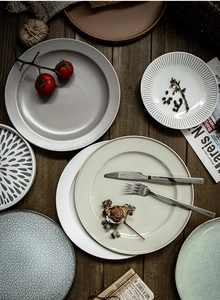 Flat lay of assorted ceramic dinner plates on dark wood with cutlery and vintage accents