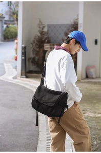 Detail of a large black canvas messenger bag featuring a secure plastic buckle and flap