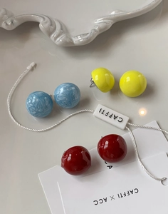Détail de boucles d'oreilles boules en émail bleu, jaune et rouge avec étiquette logo