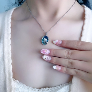 Detailed shot of an oval silver necklace with a blue rose pendant worn by a female model