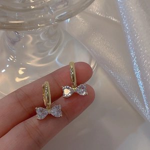 Detail of bow-shaped earrings with heart-shaped cubic zirconia in golden finish