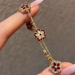 Detail of gold-plated flower bracelet featuring red and white zircon stones on a wrist