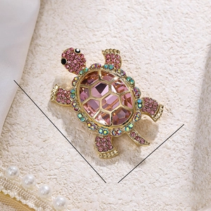 Pink crystal sea turtle brooch with gold plating and colorful rhinestones on beige fabric