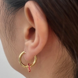Close-up of golden hoop earring with red textured detail worn by model on earlobe