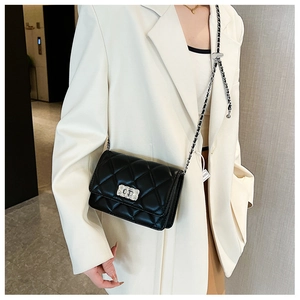 Detail of black quilted chain bag with silver lock worn on white blazer jacket