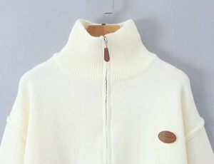 Detail of white knit cardigan showing rib-knit high collar and metallic zipper pull