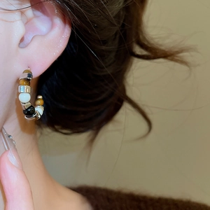 Close-up of model wearing C-shaped tiger eye bead earrings with gold accents