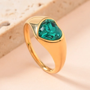 Macro shot of gold ring featuring heart-shaped green gemstone on textured stone