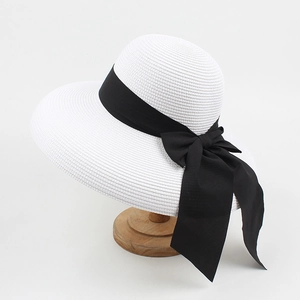 Detail of white straw sun hat with large black ribbon bow on minimalist wooden stand