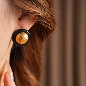 Close-up of vintage round earrings with gold hammered metal and black enamel finish