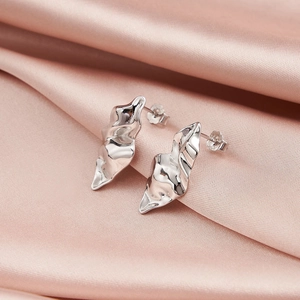 Macro detail of irregular wave-textured silver stud earrings on pink silk