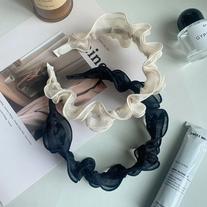 Close-up of pleated mesh headbands in cream and black on lifestyle props