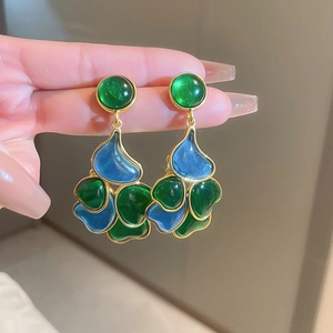 Close-up of vintage gold heart earrings with green and blue polished gemstones worn on hand
