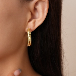 Close-up of golden multilayer hoop earrings with geometric diamond texture on a model