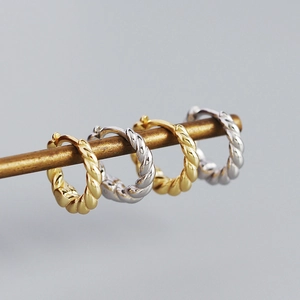 Detailed close-up of twisted hoop earrings in gold and silver finishes on a stand