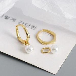 Macro view of gold hoop earrings with detachable white pearl charms on textured background