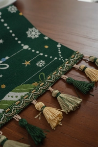Detail of Christmas table runner featuring green jacquard fabric and festive tassels