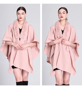 Pink knit cape featuring a plush faux fur collar and decorative pom-poms on the hem