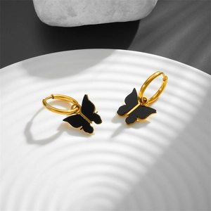 Elegant gold hoop earrings with black butterfly pendants on a textured porcelain plate
