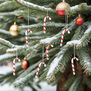 Classic red and white striped Christmas candy cane ornaments hanging on a snowy tree branch