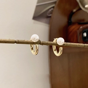 Artistic detail of gold C-shaped hoop earrings with pearls hanging on a twig branch