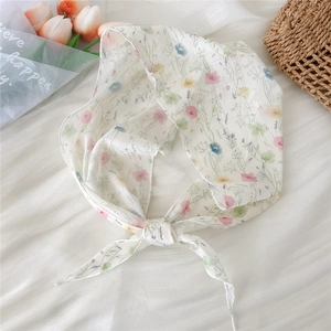 Floral print lightweight neck scarf and ribbon tied on a straw bag with tulips background