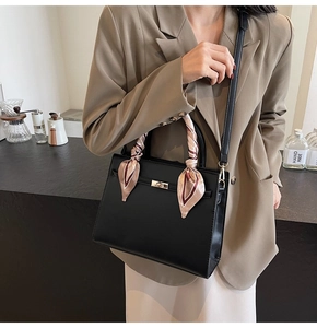 Detail of black leather handbag with gold twist lock and stylish silk scarf on handle