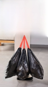 Detail of extra thick black drawstring trash bags with strong red handles and heavy load capacity