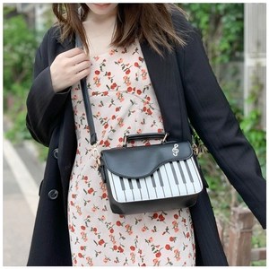 Detail of piano key themed crossbody bag with musical note metal charm worn by a model outdoors
