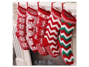 Five knitted Christmas stockings with reindeer and snowflake patterns hanging on white fireplace