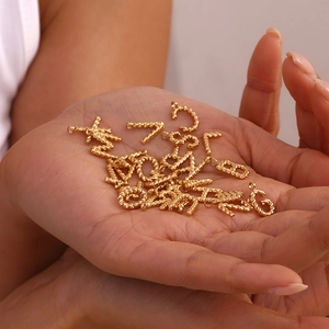 Close-up of gold twist texture letter pendants held in hand with macro details
