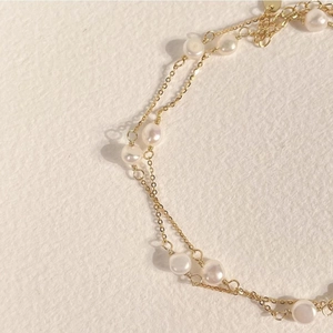 Detail of elegant pearl bead and gold metal chain necklace on textured cream background