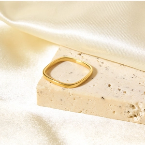 Macro view of gold square ring on beige stone texture with cream satin background