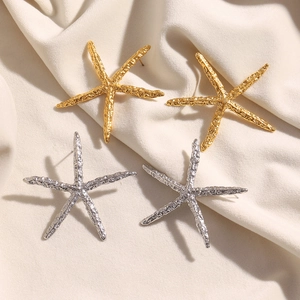 Dettaglio di orecchini a stella marina oro e argento con texture su tessuto beige