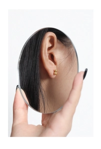 Creative mirror reflection showing a golden bear stud earring on ear with high gloss finish