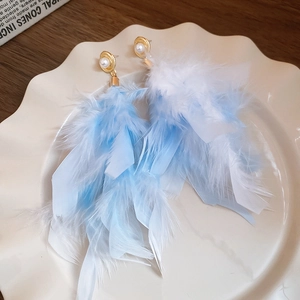 Detail of blue feather drop earrings with pearls on a decorative white ceramic tray