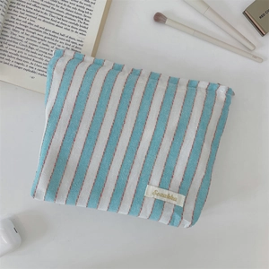 Detail shot of a blue striped canvas tote bag showing the zipper and brand label on a desk