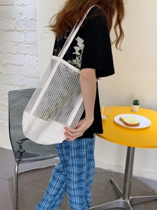 White mesh hollow tote bag with canvas bottom shown by model in a minimalist lifestyle setting