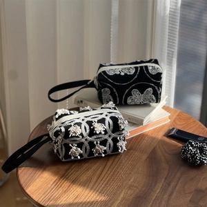 Detailed embroidery on black canvas pouch with white floral patterns and tassels