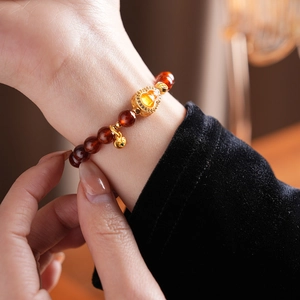 Detail of beaded garnet bracelet with golden heart charm and ruyi lock on female wrist