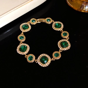 Vintage gold bracelet with emerald stones and white diamond accents on black background