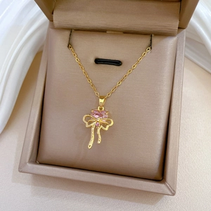 Detail of gold bow necklace with a pink heart gemstone pendant in a jewelry box