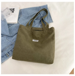 Close-up of olive green corduroy tote bag with white fashion label on a white bed
