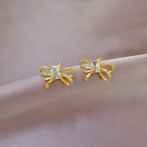Macro shot of gold bow stud earrings with square cubic zirconia on purple silk